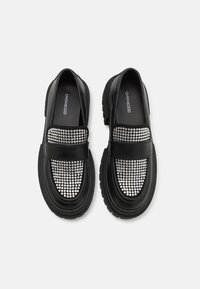 Crne ko�žne cipele na slip-on srebreni ukras sa šiljcima na prednjoj strani, s masivnom crnom gumenom potplatom i zaobljenim oblikom.