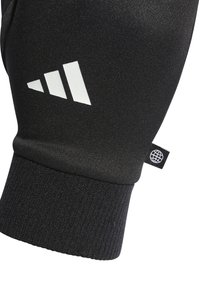 Sort atletisk handske med ribbet manchet, der har et hvidt stribet logo og en glat, mat tekstur. Holdbar og tætsiddende design.