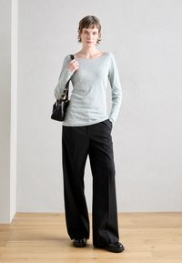 Šviesiai pilkas ilgomis rankovėmis marškinėliai, juodos plačios kelnės ir juoda rankinė. Lygus paviršius, laisvas kirpimas ir minimalizmo dizainas.