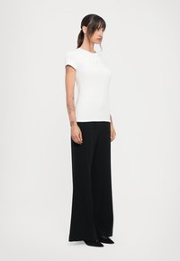 Witte korte mouwen t-shirt met reliëflogo, gecombineerd met hoge taille, wijde zwarte broek en puntige zwarte schoenen.
