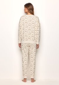 Conjunto de ropa de casa en crema con un estampado de caras de oso en toda la prenda. La parte superior tiene un corte relajado, mientras que los pantalones tienen puños de canalé. Tejido suave.