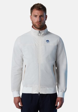 Giacca bianca con zip, caratterizzata da un colletto alto, tasche laterali e polsini elasticizzati, con un accento del logo blu sul petto. Texture liscia.