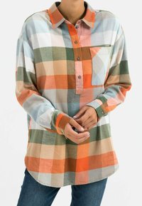 Chemise à carreaux multicolore à manches longues, avec des nuances d'orange, de vert et de beige, une patte de boutonnage et une poche poitrine devant.