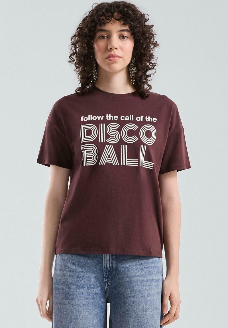 Bordeaux-rotes Baumwoll-T-Shirt mit auffälligem weißen Text, der "folge dem Ruf der DISCO-KUGEL" in verschiedenen Schriftstilen zeigt. Kurze Ärmel und Rundhalsausschnitt.