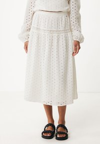 Vit midi kjol med ögonbladsdetaljer, elastisk midja och flerskiktad design. Bärs med svarta flätade sandaler.
