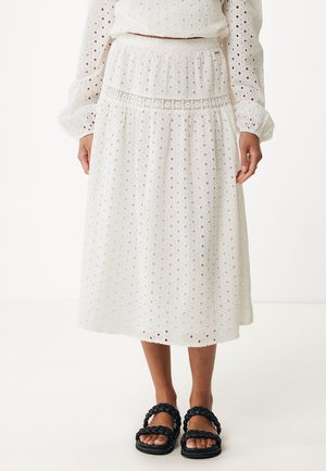 Gonna midi bianca con dettagli in pizzo, elastico in vita e design a strati. Indossata con sandali neri intrecciati.