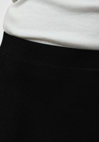 Gros plan d'une personne portant un haut côtelé blanc rentré dans un pantalon noir taille haute avec une ceinture unie.