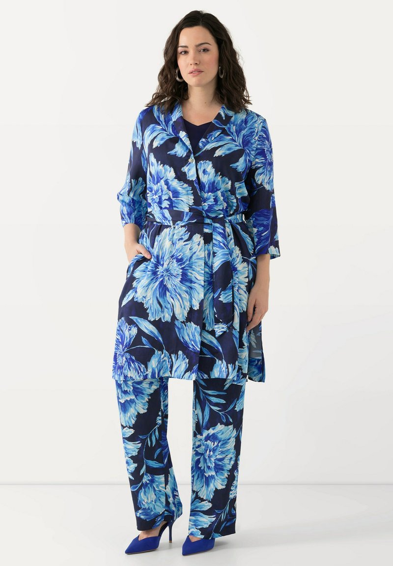 Marineblauwe outfit met een bloemenpatroon, bestaande uit een lange, met een riem gelegde jas met driekwartmouwen en bijpassende losse broek. Blauwe hoge hakken.