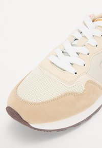 Baskets beiges avec une tige en mesh, des accents en velours, des lacets blancs et une semelle en caoutchouc texturée pour une meilleure adhérence. Forme arrondie.