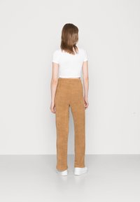 Calças castanhas de cintura alta, texturizadas, com um design de perna reta. Combinadas com uma camisa justa branca de mangas curtas e ténis brancos.