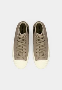 Beige high-top sneakers made of textured material. Features cream rubber toe cap and beige laces. Black accent on the side.