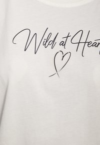 Weißes Baumwoll-T-Shirt mit schwarzem Schriftzug "Wild at Heart" und einem Herz-Graphic, mit runden Halsausschnitt und glatter Textur.