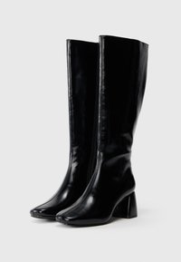 Melnas ceļgala augstās kurpes, izgatavotas no spīdīga āda, ar bloku papēdi un norādītu pirksta dizainu, gludu tekstūru un redzamām vīlēm.