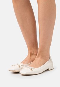 Weisse Lederballetschuhe mit runder Zehenpartie, die mit einer kleinen Schleife und goldenen Akzenten verziert sind, auf einem niedrigen Blockabsatz.