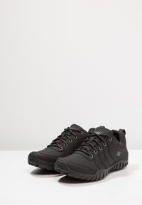 Scarpe da ginnastica nere con un design elegante, realizzate in materiale sintetico, lati texturizzati e suola in gomma. Lacci con occhielli metallici.