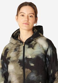 Chaqueta acolchada con capucha en un estampado de acuarela que presenta tonos de oliva, negro y crema. Tiene un cierre frontal de cremallera y patrones texturizados en forma de ola.