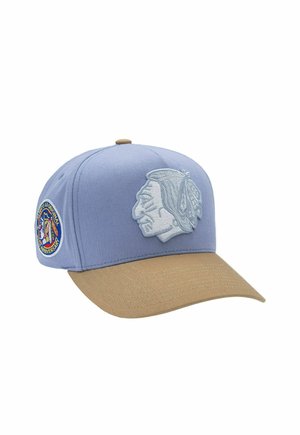 Blue and tan baseball cap with embroidered Native American profile on front and circular patch on side.