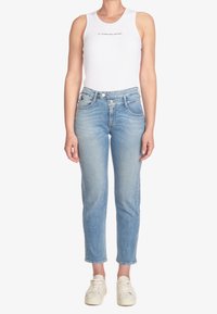 Weißes, geripptes Tanktop mit Text, kombiniert mit hellblauen Jeans. Sneakers in neutraler Farbe, die ein lässiges Outfit-Design zeigen.