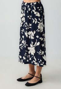 Midikleid mit floralen Muster in Marineblau mit weißen Blumen, ausgestattet mit einem elastischen Bund. Kombiniert mit schwarzen Ballerinas.