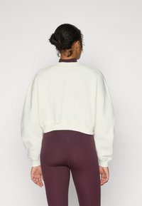 Kuttet, kremfarget sweatshirt med drop shoulders og ribbede detaljer, kombinert med figurnære burgunder leggings. Glatt tekstur, enkel design.