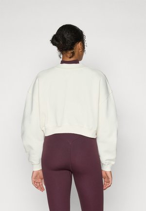 Afgekorte, crèmekleurige sweatshirt met afhangende schouders en ribgebreide accenten, gecombineerd met strakke bordeauxrode legging. Vlotte textuur, eenvoudig ontwerp.