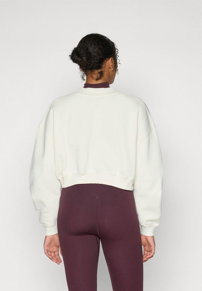 Kuttet, kremfarget sweatshirt med drop shoulders og ribbede detaljer, kombinert med figurnære burgunder leggings. Glatt tekstur, enkel design.