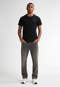 Camiseta negra de algodón con mangas cortas, combinada con vaqueros gris desgastados y zapatillas blancas. Diseño sencillo, cuello redondo y sin estampados visibles.