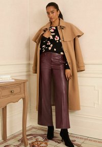 Kamieļa pārnēsās mētelis, melna ziedu džemperis un bordeļa mākslīgās ādas plati legi bikses, apvienotas ar melniem papēžu potīšu zābakiem.