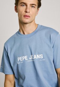 Light blue cotton t-shirt featuring white text "PEPE JEANS" and additional branding details. Short sleeves and crew neckline.