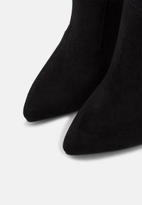 Botines de ante negro hasta el tobillo con punta afilada. Textura suave y diseño sencillo, sin herrajes ni adornos visibles.
