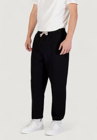 Zwarte sweatpants met een trekkoord in de taille, taps toelopende pijpen en geribbelde boorden, gecombineerd met witte sneakers en een eenvoudig wit t-shirt.