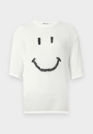 Pull court blanc en maille avec un visage souriant noir brodé sur le devant, doté d'un col rond et d'une texture en maille.