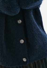 Jersey de punto navy con un acabado texturizado, que presenta tres botones metálicos en forma de flor en la parte delantera.