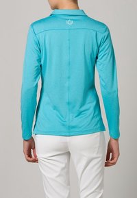 Turkos långärmad polo tröja med krage, rak passform och en minimalistisk design med små vita prickar på övre ryggen.