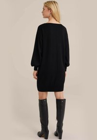 Must team is a black knitted dress with a loose fit, long puff sleeves, and ribbed hem. It is paired with tall black leather boots featuring a zipper.