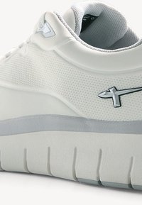 Fehér sneaker, mely texturált felülettel, párnázott nyakkal és ezüst logó részlettel rendelkezik. A talp réteges, vastag dizájnú, bemélyedésekkel ellátva.