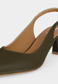 Γυναικείο παπούτσι slingback σε ελιά πράσινο με μυτερή μύτη, ταμπά εσωτερική επένδυση και χοντρό τακούνι σε λευκό φόντο.