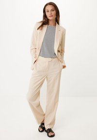 Blazer beige e pantaloni larghi abbinati a una camicia a righe. Tessuto morbido, vestibilità rilassata e sandali neri con un design chunky.