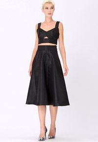 Ensemble noir en deux pièces comprenant un haut court avec une découpe et des bretelles larges, associé à une jupe fluide, à hauteur des genoux, en finition satinée.