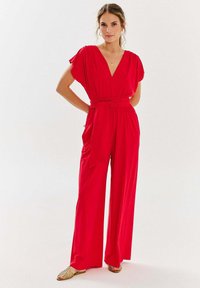 Czerwony kombinezon z głębokim dekoltem w kształcie litery V, krótkimi rękawami i wiązanym w pasie. Wykonany z gładkiego materiału, z szerokimi nogawkami i luźnym krojem.