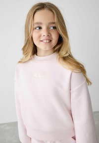Ljusrosa sweat-shirt med ribbad krage och muddar, med guldtexten "BAKER by Ted Baker" på framsidan. Mjukt material, avslappnad passform.