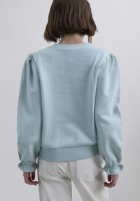 Suéter azul claro con mangas abullonadas y puños acanalados. Tejido suave con un corte relajado y cuello redondo. Diseño simple con detalles mínimos.