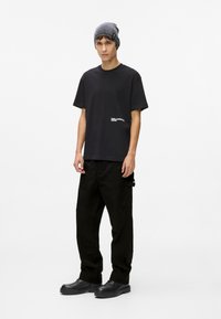 Tricou negru cu mâneci scurte și un logo alb, asortat cu pantaloni cargo negri cu buzunare. Accesoriile includ o căciulă tricotată gri.