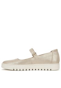 Chaussure en cuir synthétique beige avec un bout rond, une sangle réglable et une semelle en caoutchouc texturé blanc présentant des rainures horizontales.