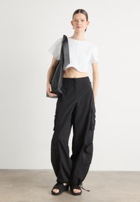 Λευκό κοντομάνικο μπλουζάκι με καλλυντική εφαρμογή, μαύρο cargo παντελόνι με τσέπες και άνετη εφαρμογή, και μαύρες πλατφόρμες σανδάλια.