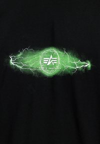 Černé tričko s centrální grafikou: zelené bleskové efekty obklopující kruhové logo s textem "ALPHA INDUSTRIES" v bílé barvě.
