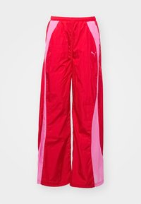 Pantalon de sport large rouge et rose avec taille élastique et logo Puma sur la cuisse droite, sur fond blanc.