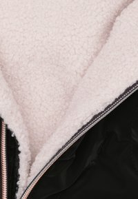 Zwarte jas met een lichtroze fleece voering. Voorzien van een ritssluiting en een gladde buitenkant. Geaccentueerd met een contrasterende rits.