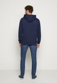 Navyblauwe hoodie met een trekkoordkap, geribbelde manchetten en een kangoeroezak, gecombineerd met blauwe denim jeans en casual schoenen.
