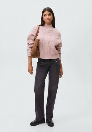 Pull en tricot rose clair avec une texture côtelée, associé à un jean gris foncé avec des clous sur les côtés et des chaussures à plateforme noires. Sac marron.